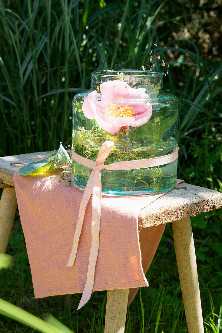 Glass vase with pink flower on wooden stool in the garden