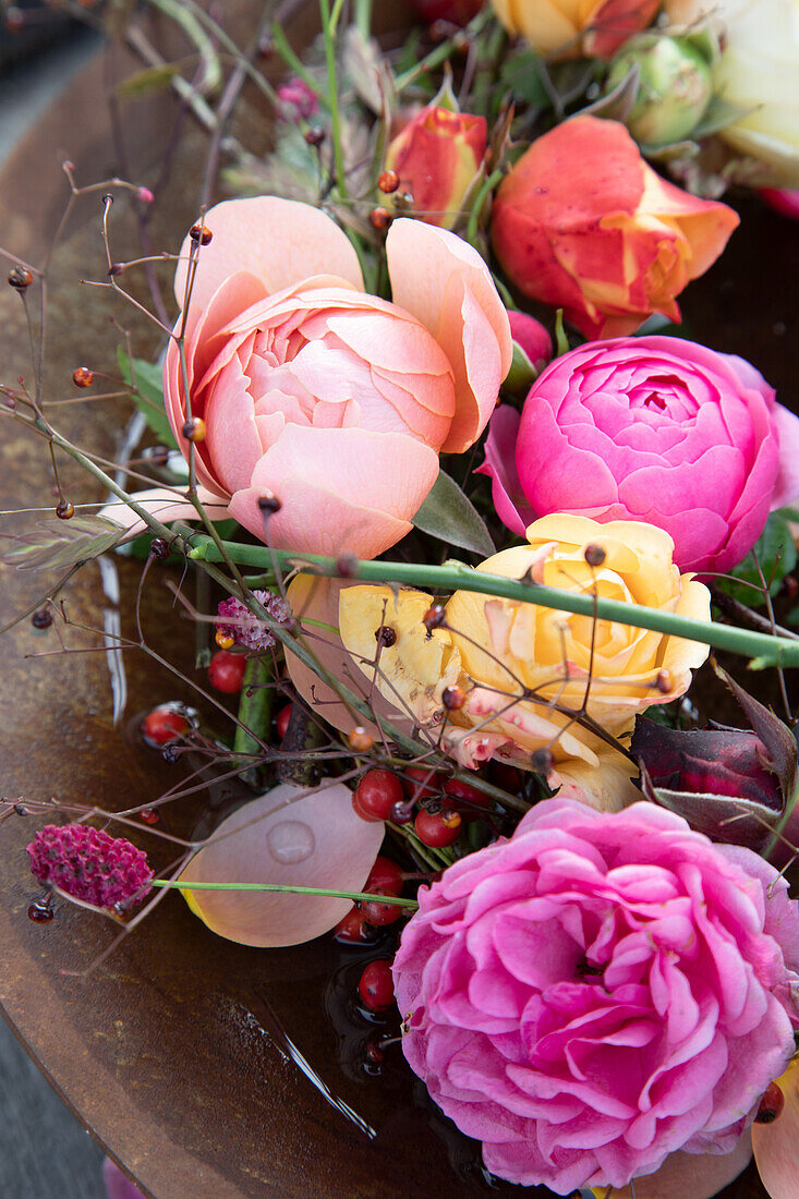 Ranunkeln (Ranunculus) und Rosen in verrosteter Schale