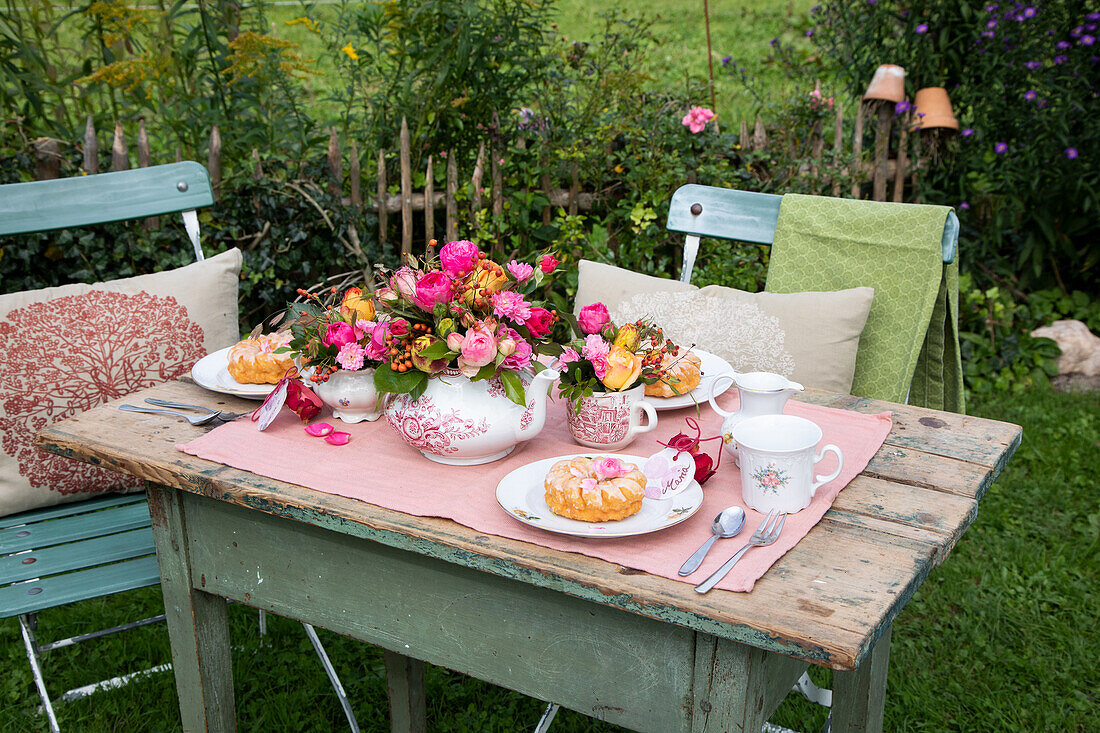 Gedeckter Gartentisch mit Blumengedeck und Gebäck im sommerlichen Garten