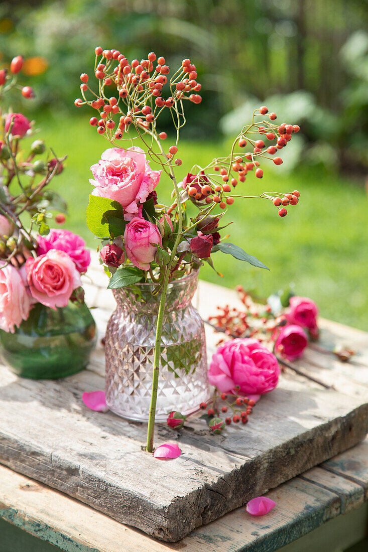 Rosenstrauß in Kristallvase auf rustikalem Holztisch im Sommergarten