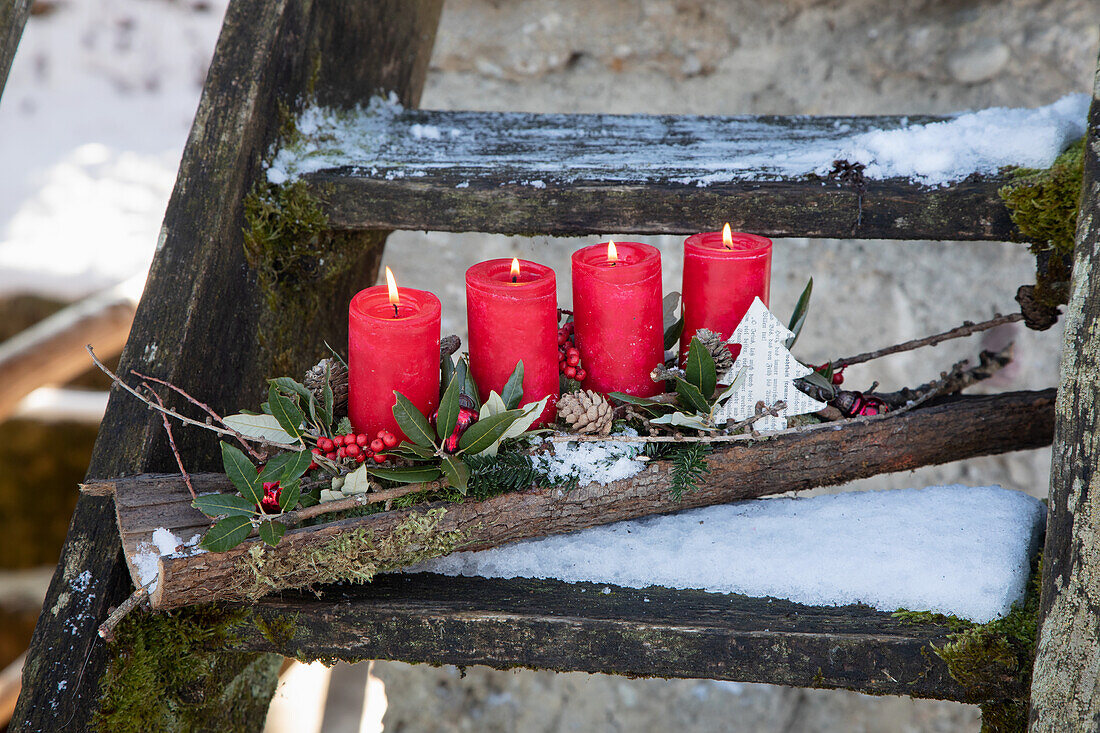 Weihnachtliche Dekoration mit vier roten Kerzen auf verschneiter Holztreppe