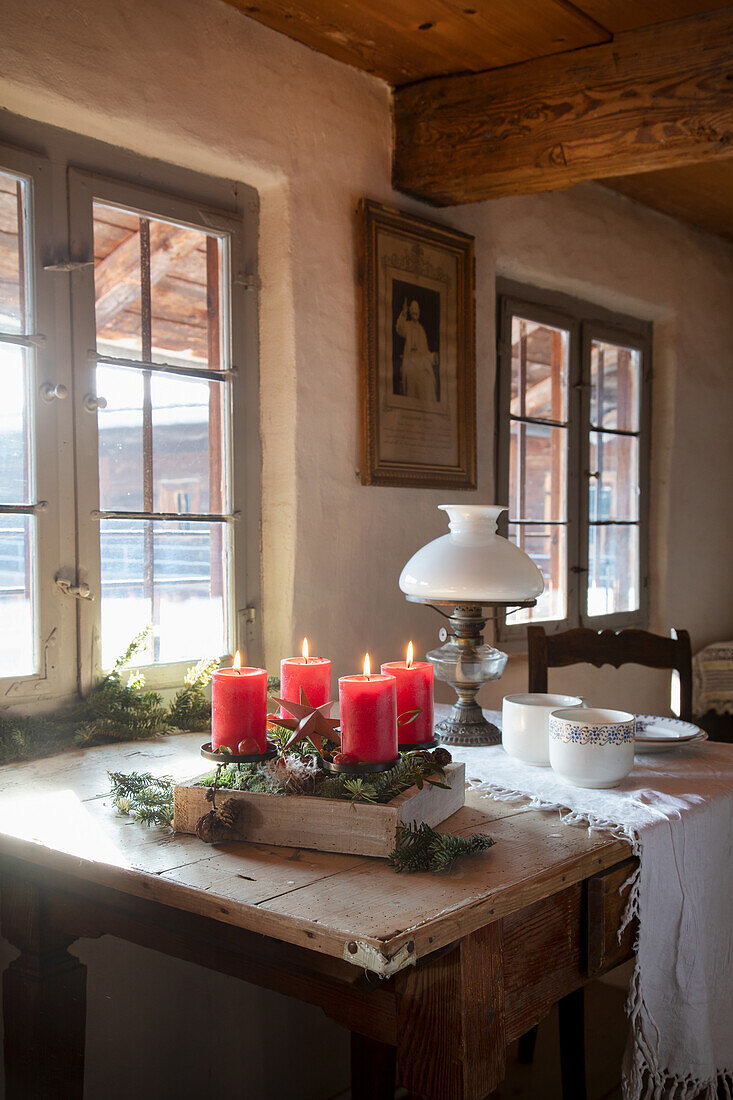 Holztisch mit Adventskranz und brennenden roten Kerzen vor Sprossenfenstern