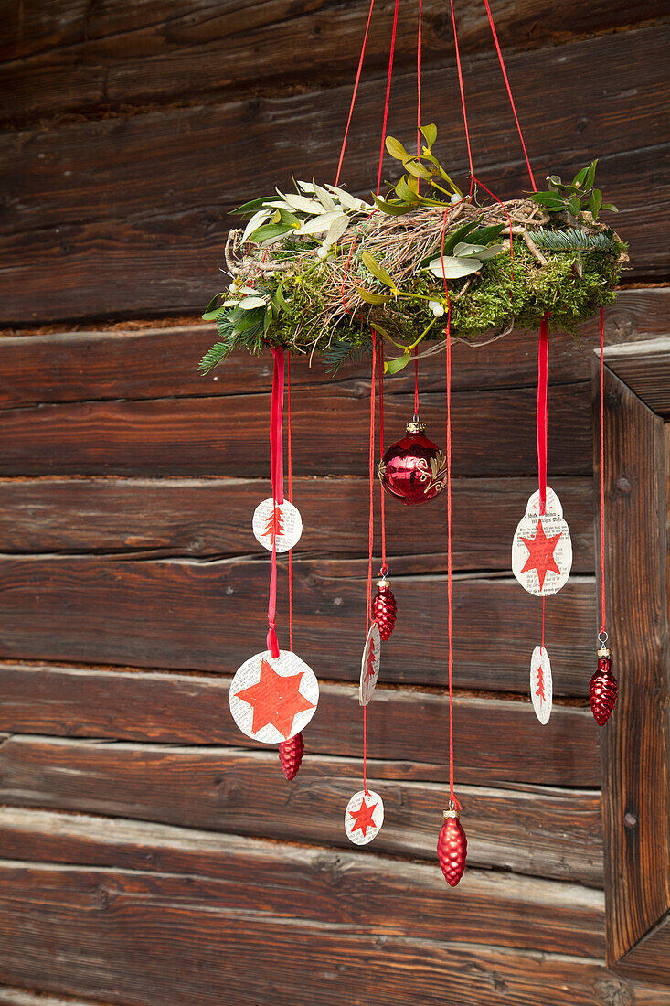 Adventskranz mit roten Sternanhängern vor Holzhütte