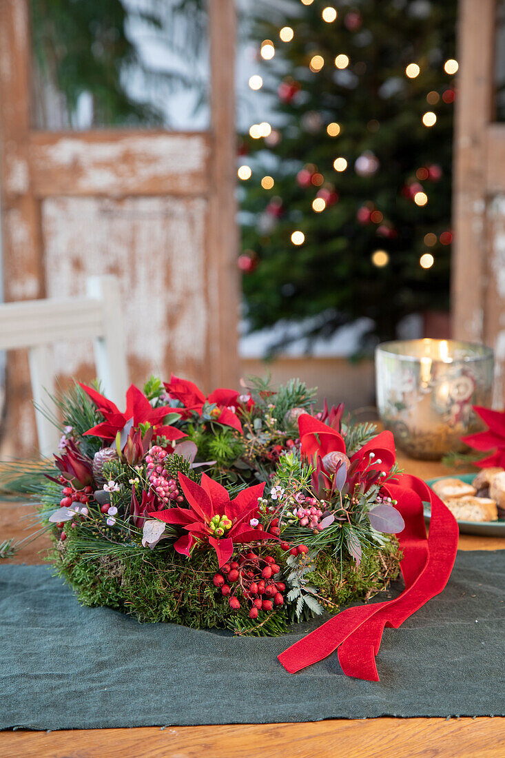 Weihnachtlicher Kranz mit Stechpalmen, Beeren und Schleife auf Holztisch