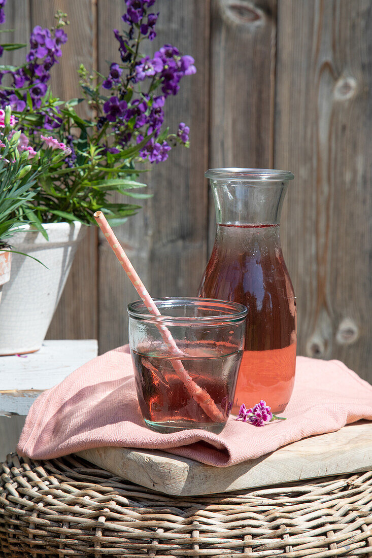 Glas und Karaffe mit sommerlichem Erfrischungsgetränk auf Rattan-Tisch