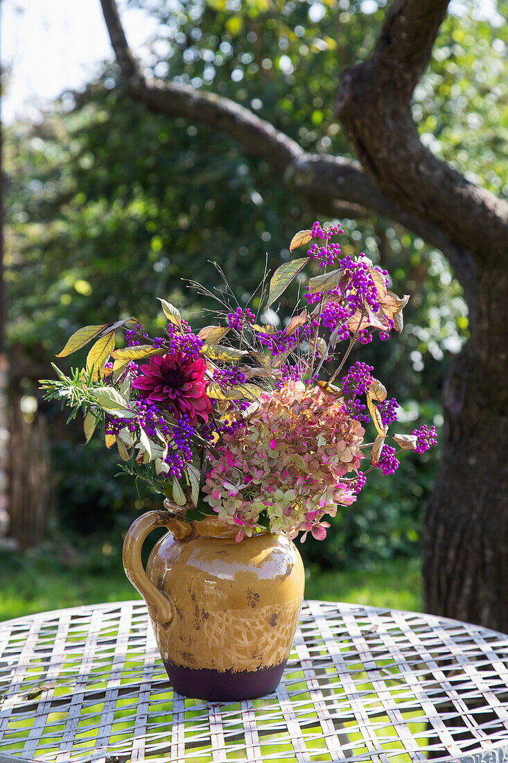 Gartenblumenstrauß in gelber Tonvase auf Gartentisch im Spätsommer