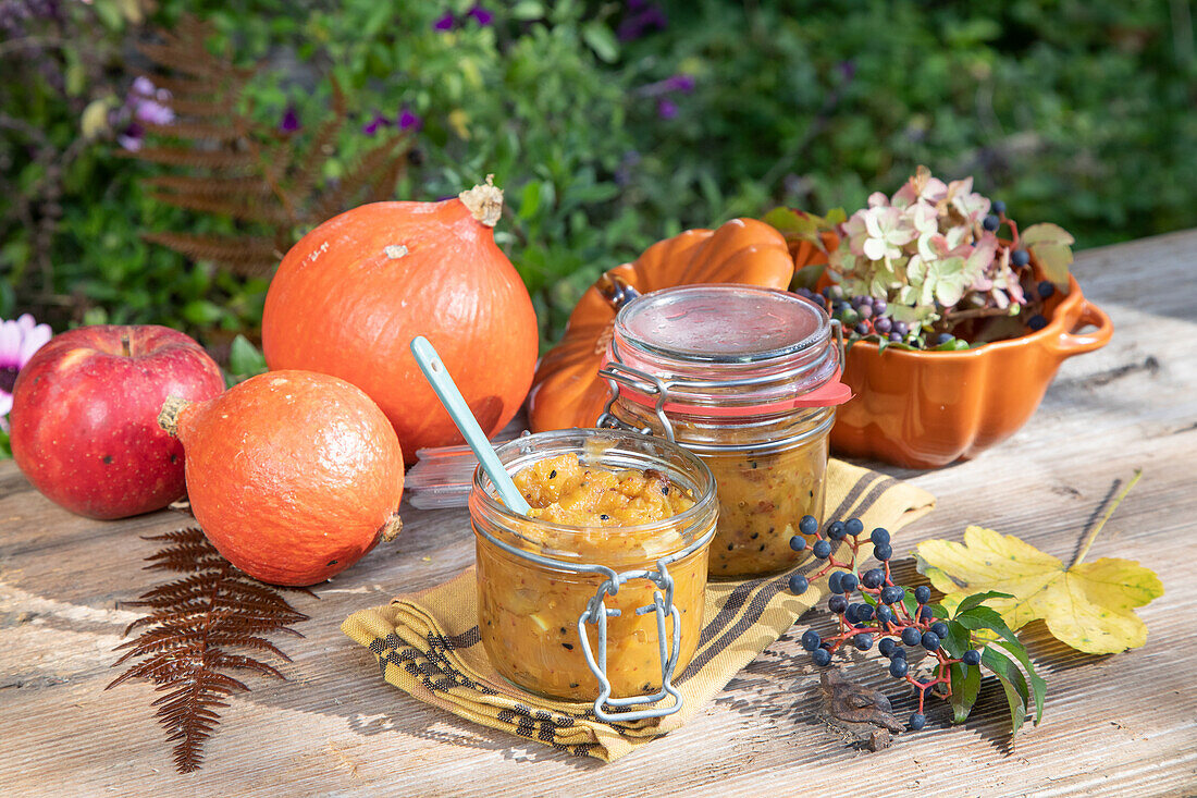 Homemade pumpkin jam on a wooden table in the garden, decorated with ornamental pumpkins and autumn leaves