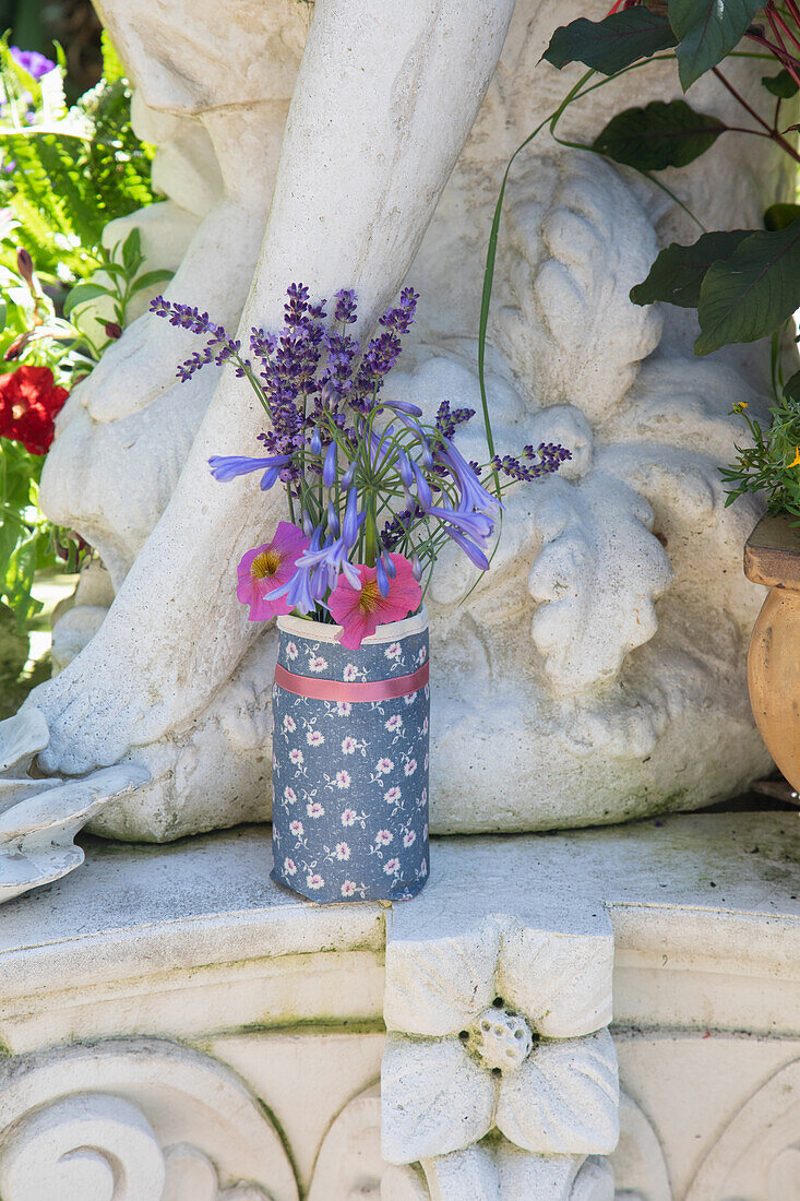 Wildblumenstrauß in dekorierter Vase vor Steinskulptur im Garten