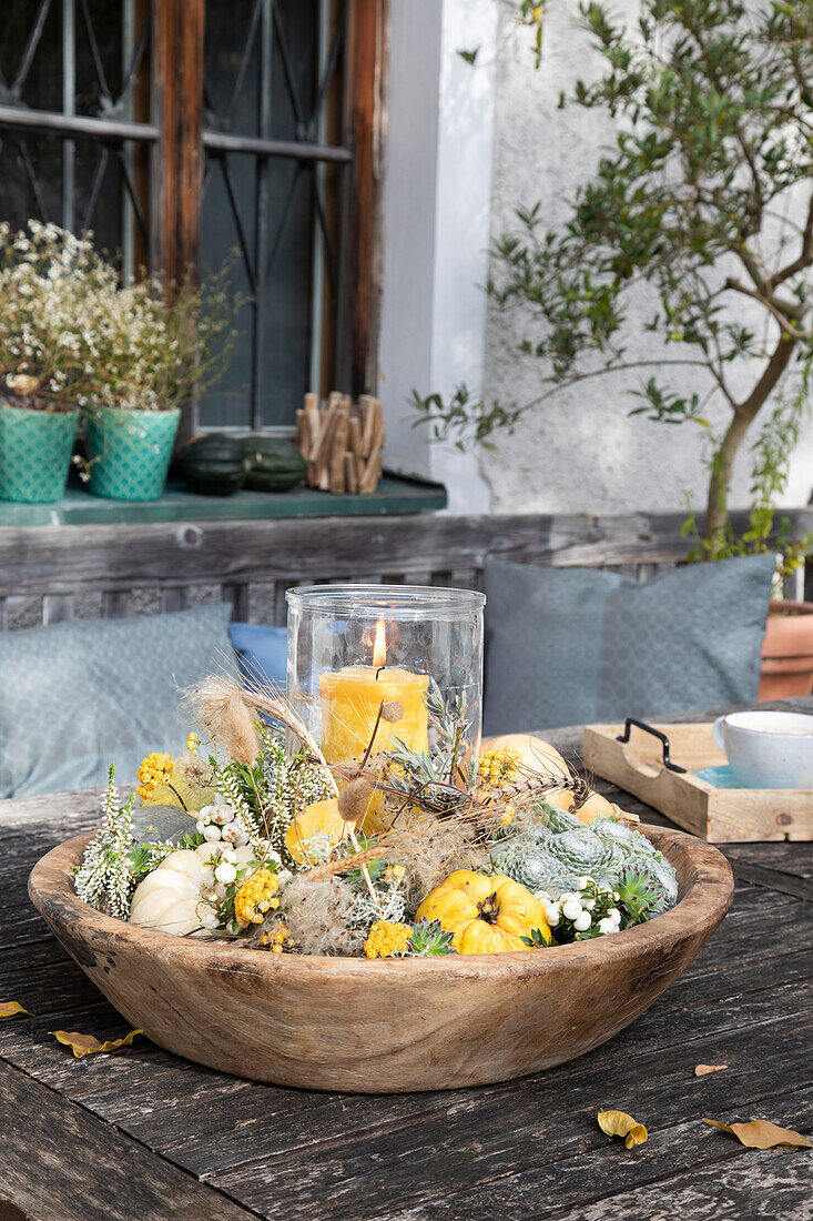 Autumnal table decoration with pumpkins, candle and dried flowers in a wooden bowl