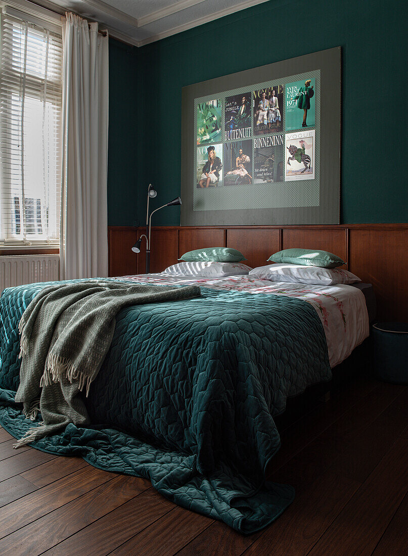 Doppelbett mit dunkelgrüner Tagesdecke und Postercollage im Schlafzimmer