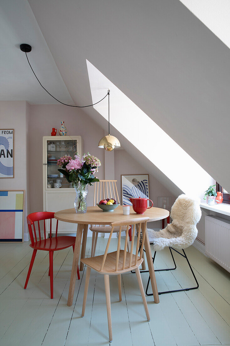 Dining area under a sloping roof with wooden and metal chairs, bouquet of flowers and fruit bowl