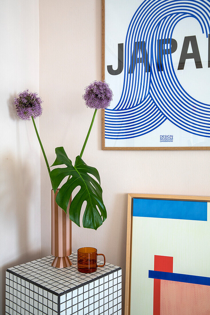 Monstera-Blatt und violette Allium-Blüten in Vase auf gefliestem Beistelltisch