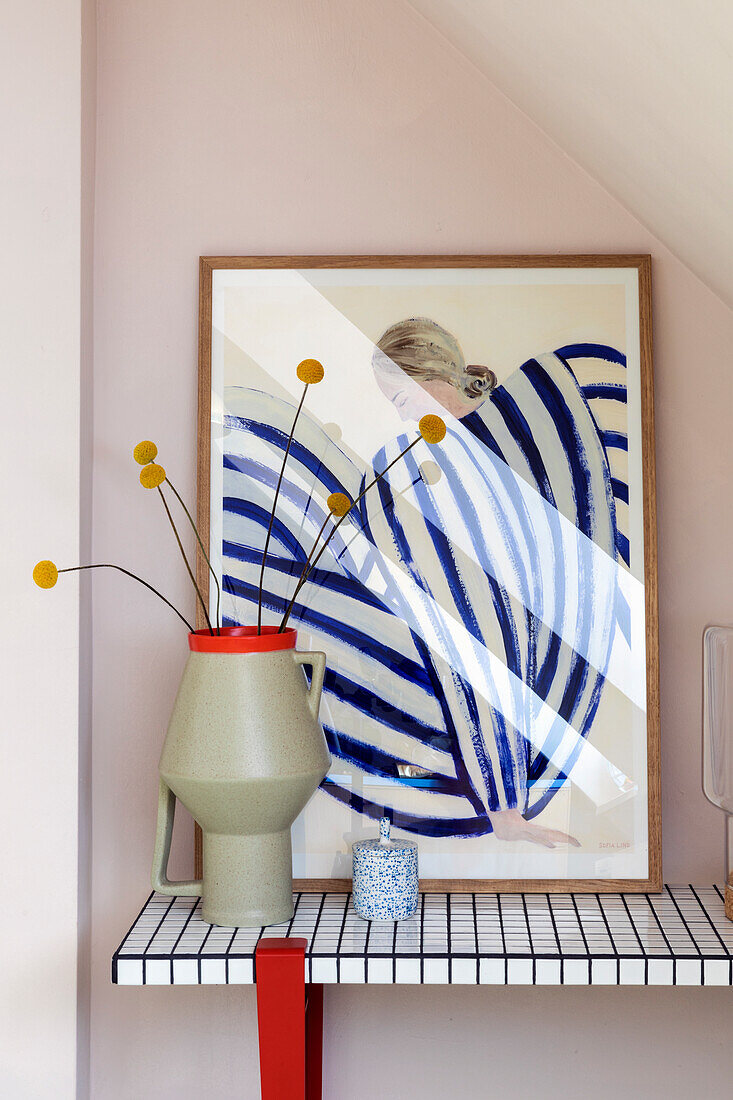 Graphic artwork on grid shelf with ceramic vase and yellow flower stems