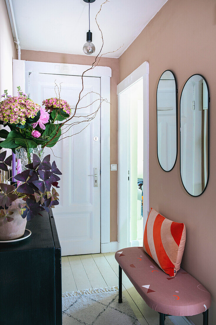 Narrow hallway with floral arrangement, upholstered bench and oval mirrors