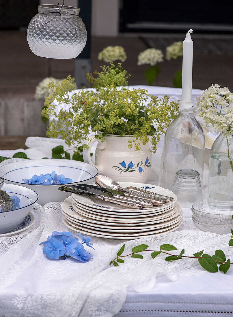 Gedeckter Gartentisch mit Porzellantellern, Blumen und weißen Spitzendecken