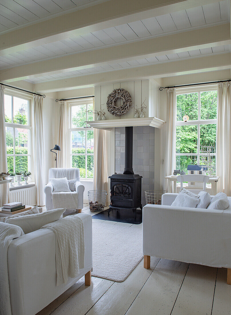 Living room with wood-burning stove, light-coloured fabric sofas and large windows