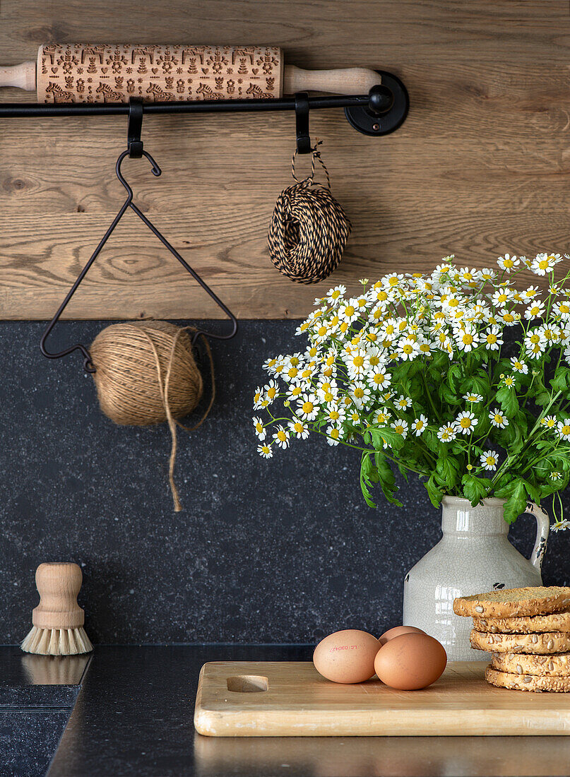 Küche mit Holzdetails, Kamille in Vase, Gebäck und Eier auf Schneidebrett