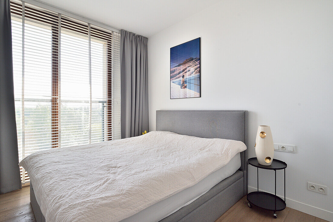 Schlafzimmer mit Doppelbett, Nachttisch und Jalousien in Warschauer Apartment