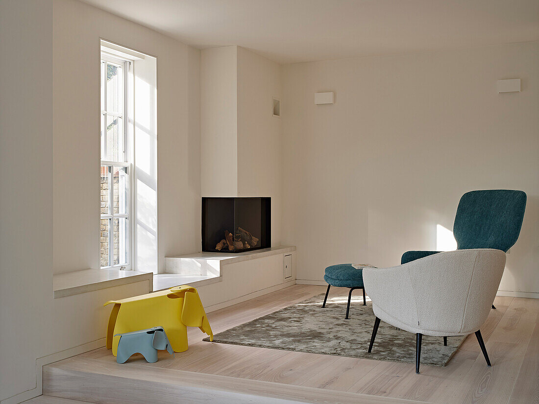 Seating area with upholstered armchairs, fireplace and designer children's toys by the window, modern interior