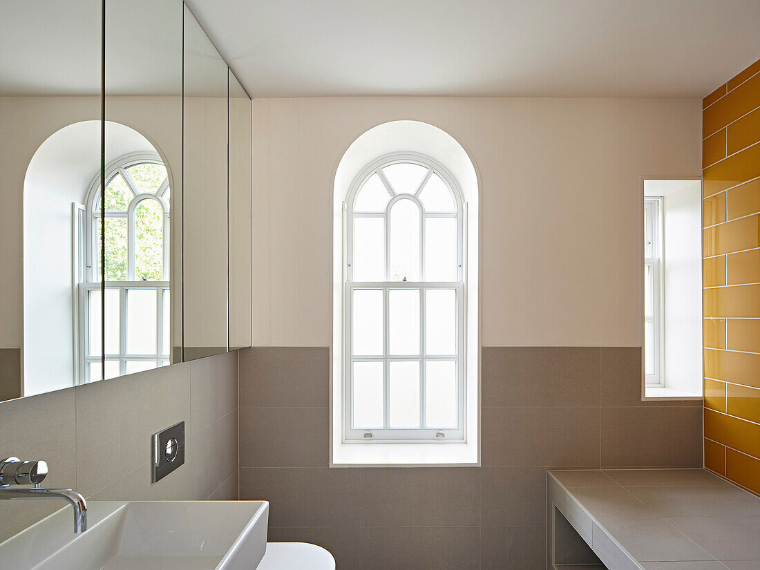 Badezimmer mit Spiegel und Rundbogenfenster, gelb geflieste Wand
