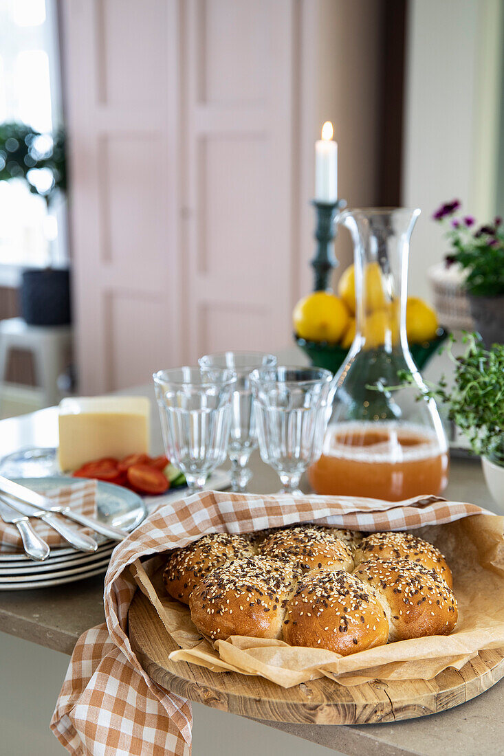 Gedeckter Tisch mit Brötchen, Glaskaraffe mit Saft und Käse