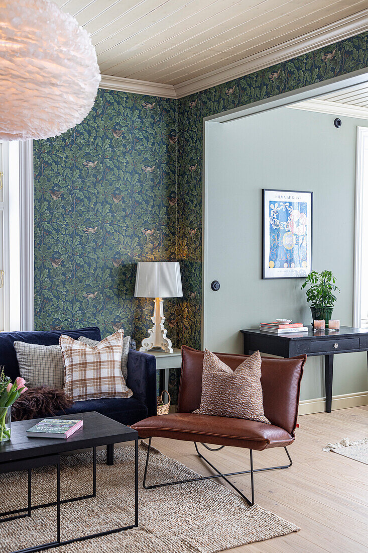 Living room with patterned wallpaper, brown leather armchair and dark sofa