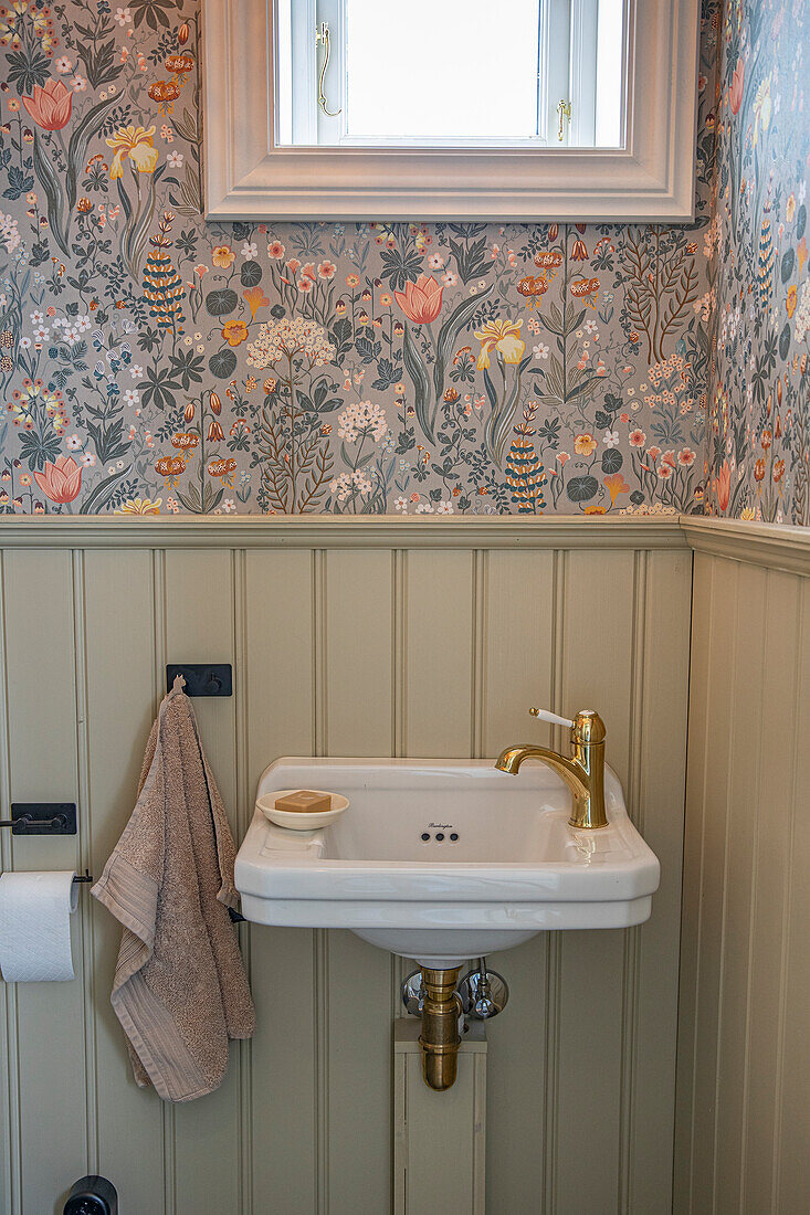 Guest WC with floral wallpaper and small washbasin with golden fittings