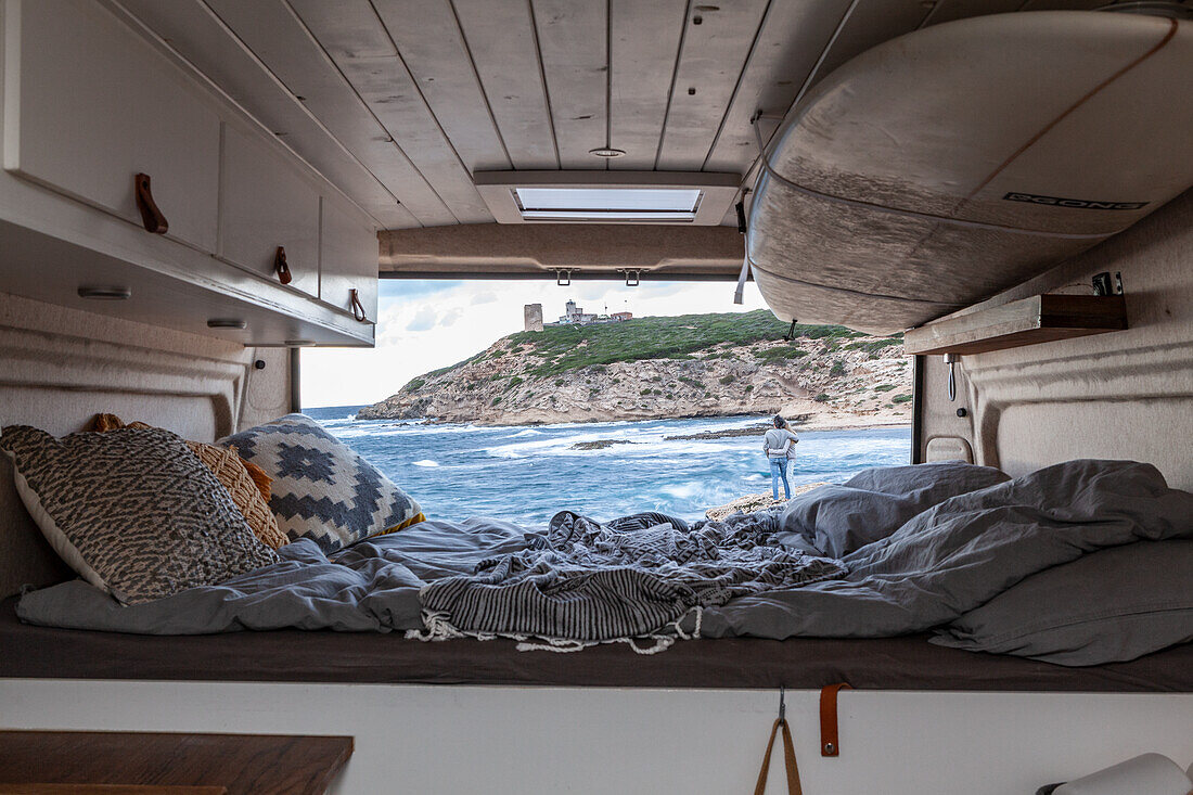 Cosy interior of a van with bed and surfboard on the beach