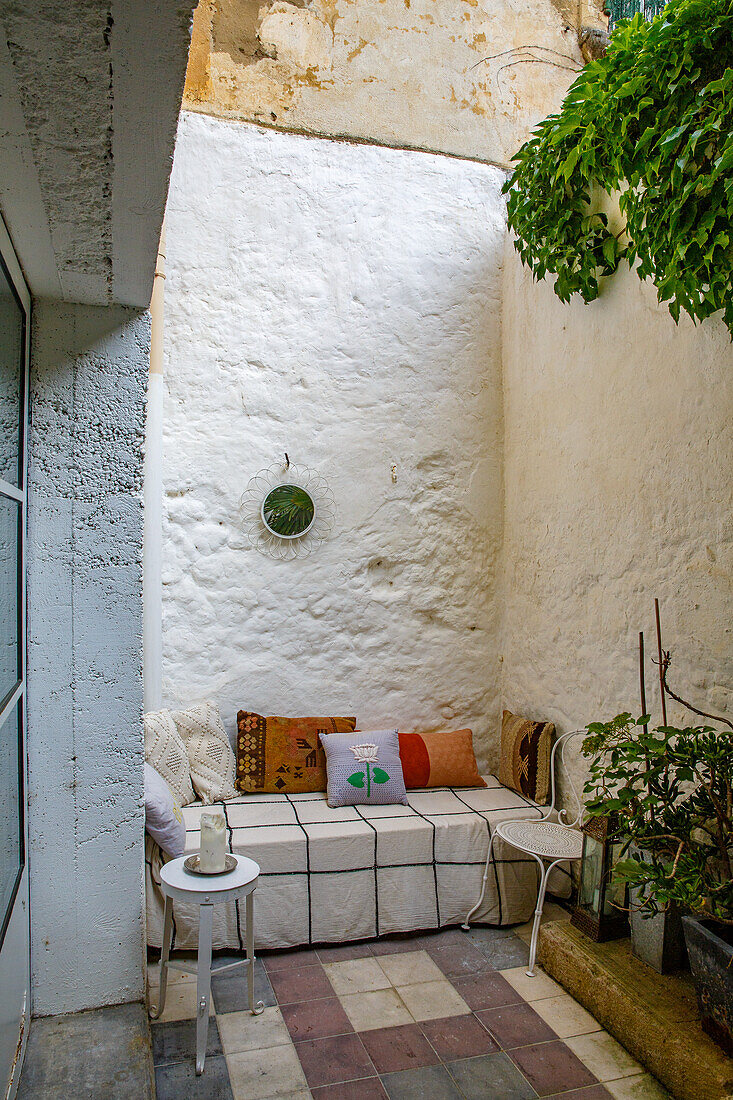 Small patio with seating area, white side tables and cushions on the bench