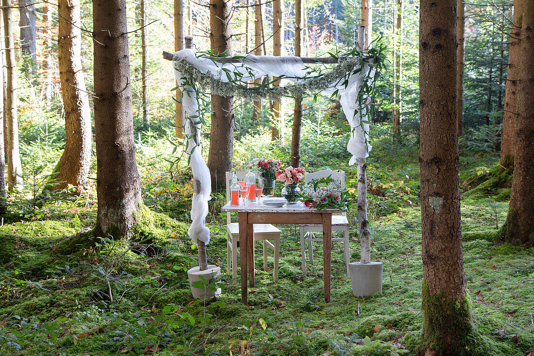 Rustikaler Hochzeitstisch unter Baldachin im Wald mit Blumen und Kerzen