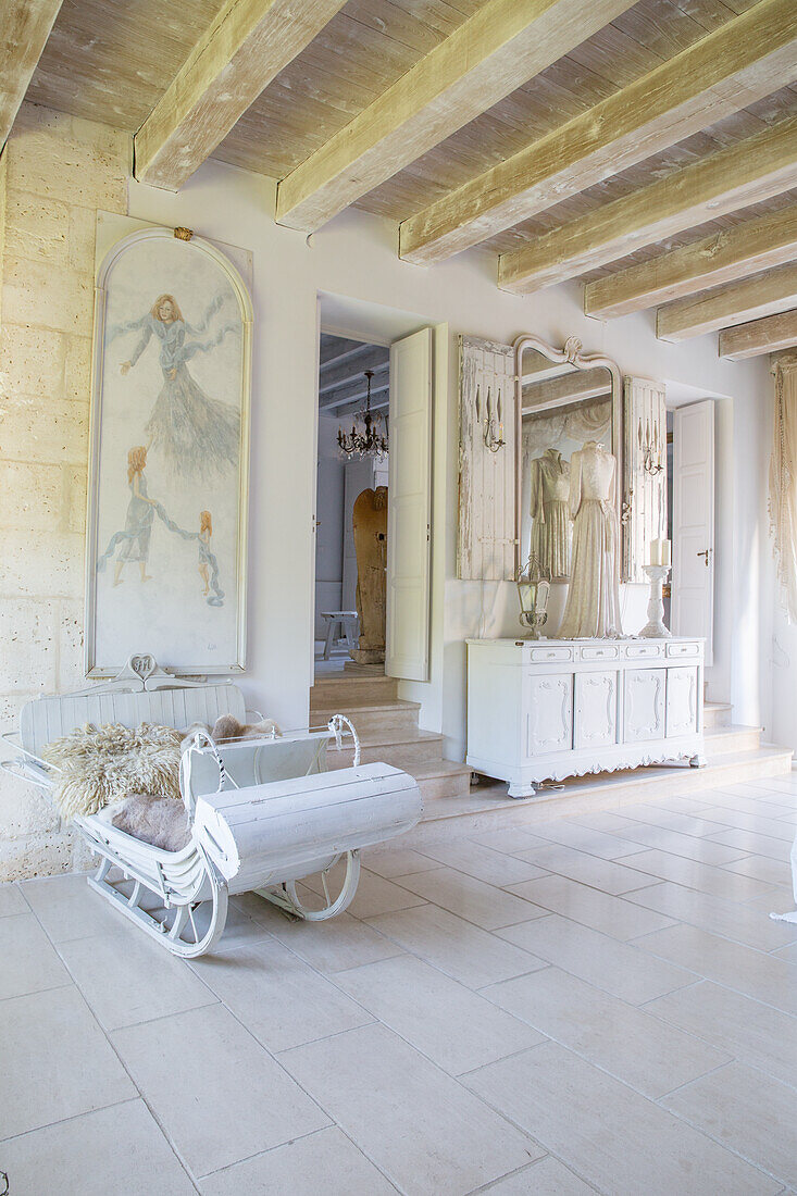 Bright hallway with antique, white-painted sleigh and large wall mirrors