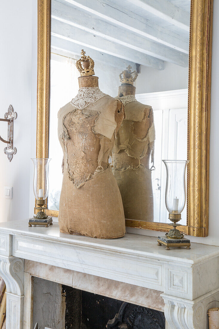 Historic dressmaker's dummy with crown in front of mirror on marble fireplace