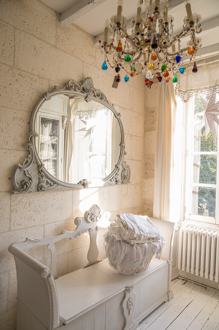 Antique mirror with ornate frame in bright, romantic room with crystal chandelier and bench seat