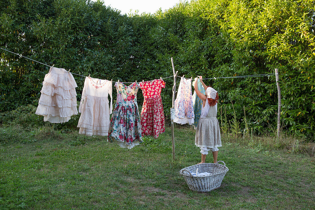 Woman hangs vintage summer dresses on washing line in the garden