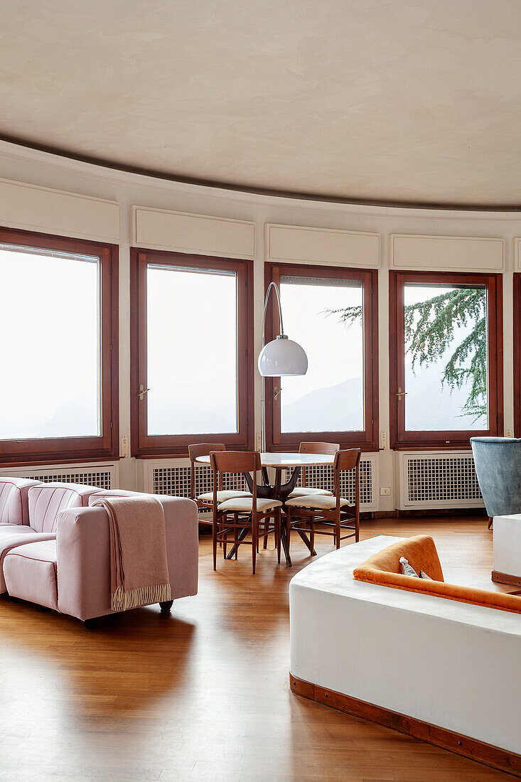 Round living room with lots of windows, round dining table and pink sofa