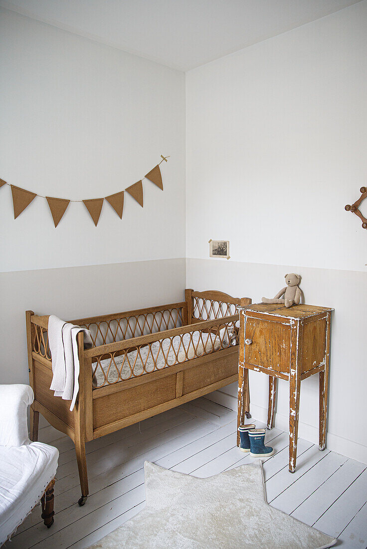 Babyzimmer mit Holzgitterbett, Vintage-Nachttisch und Wimpelkette an der Wand