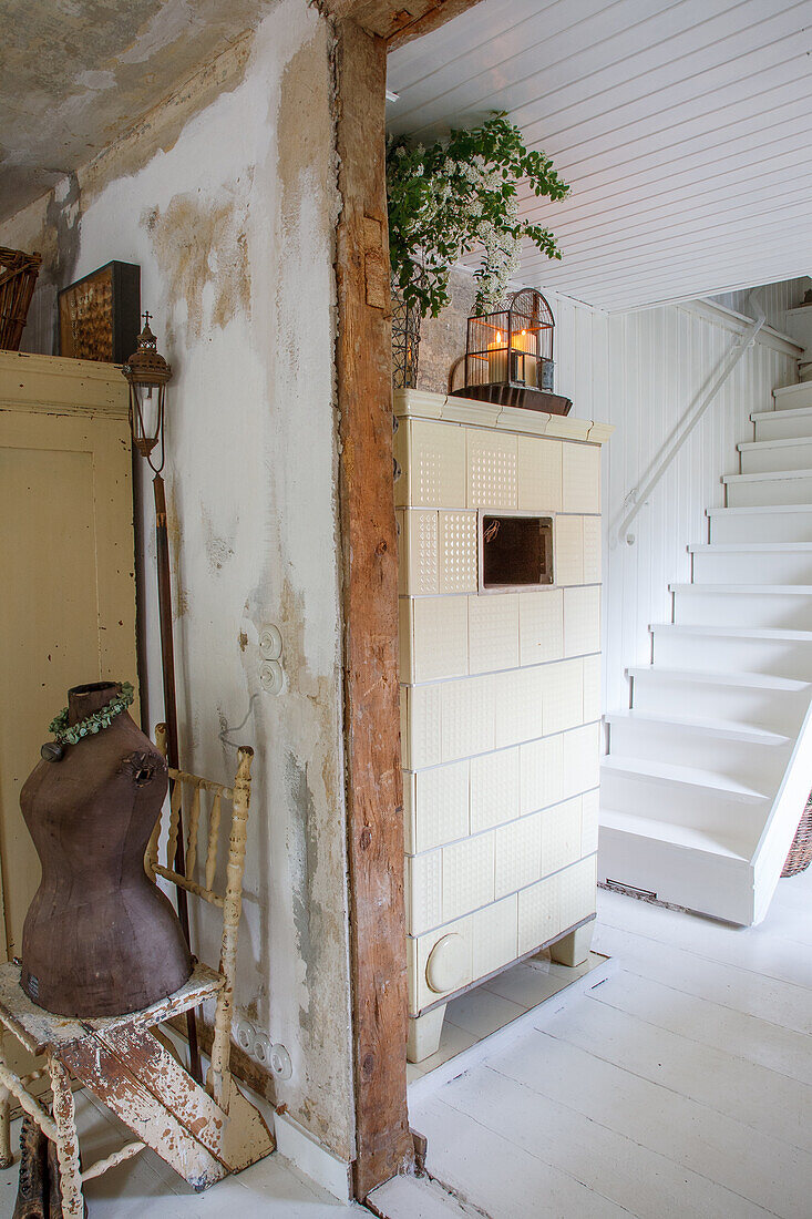 White tiled stove and dressmaker's dummy in front of staircase