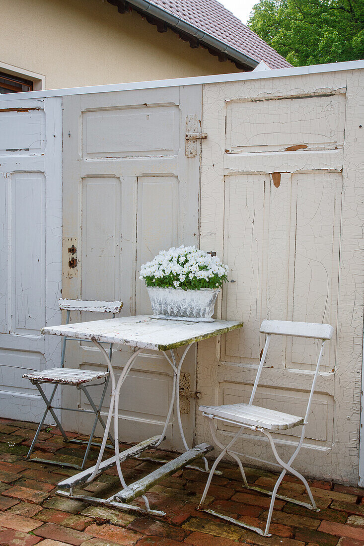 Small seating area with white metal chairs and table in front of old wooden doors