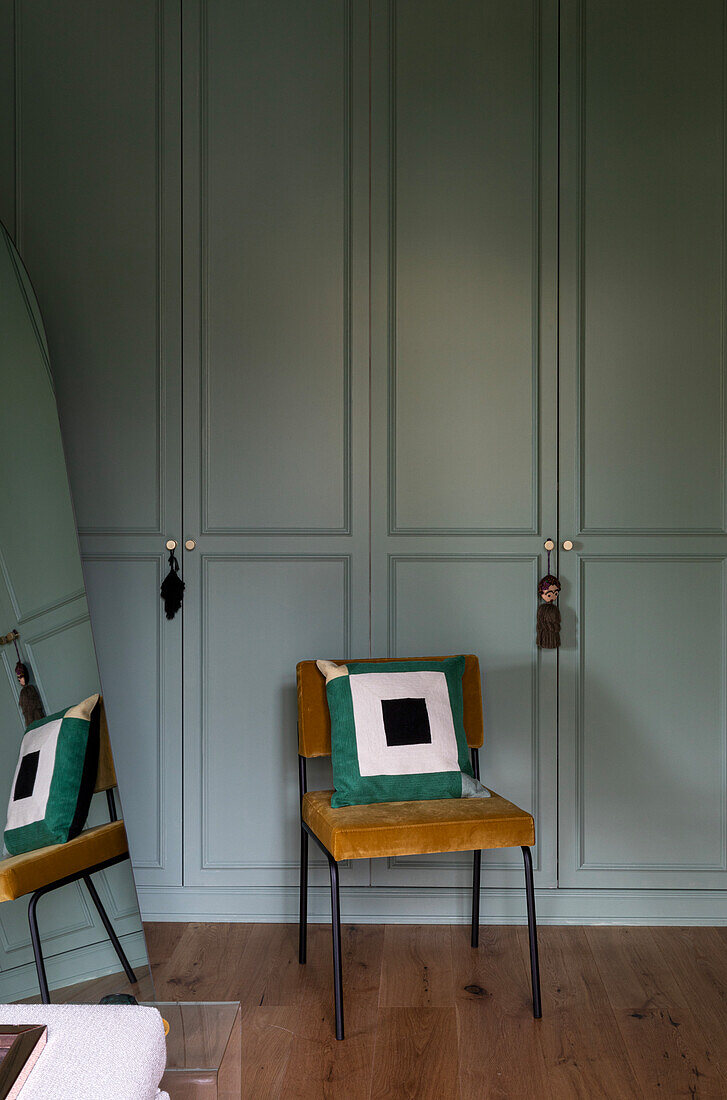 Mustard yellow velvet chair in front of pastel green built-in wardrobe in bedroom