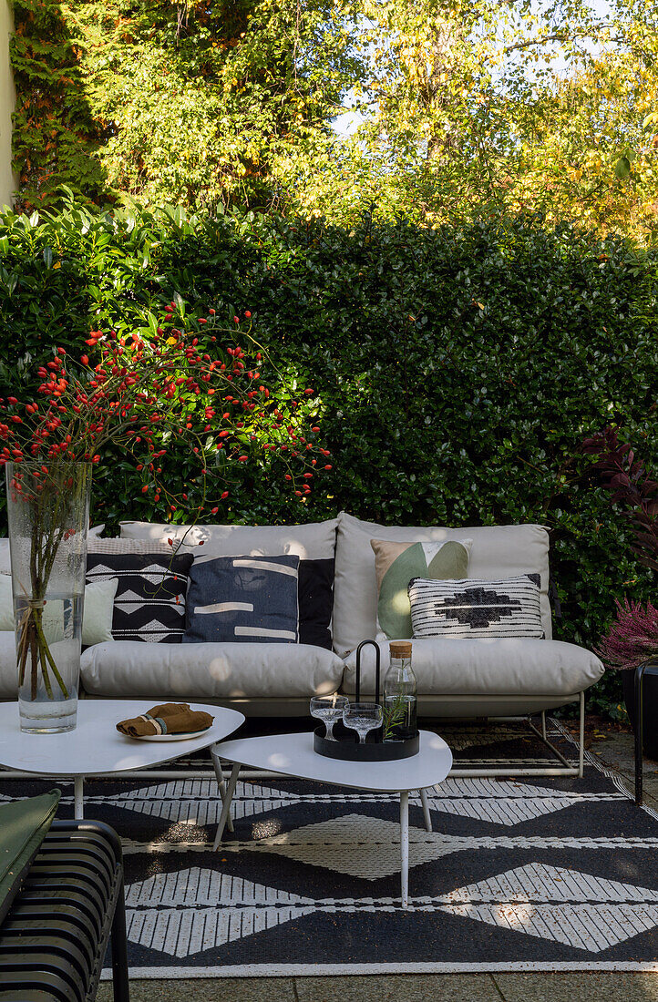 Moderne Terrasse mit weißem Sofa, gemusterten Kissen, Outdoor-Teppich und Couchtischen