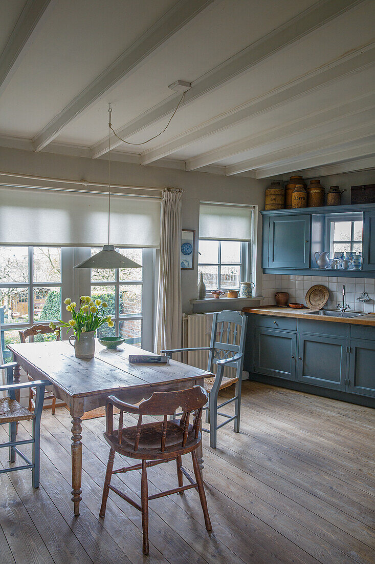 Wooden kitchen with blue cupboards, dining table and bouquet of flowers