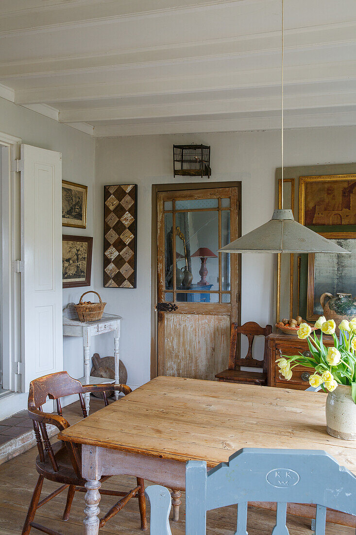 Dining area with rustic wooden table, chairs, bouquet of tulips and antique decoration