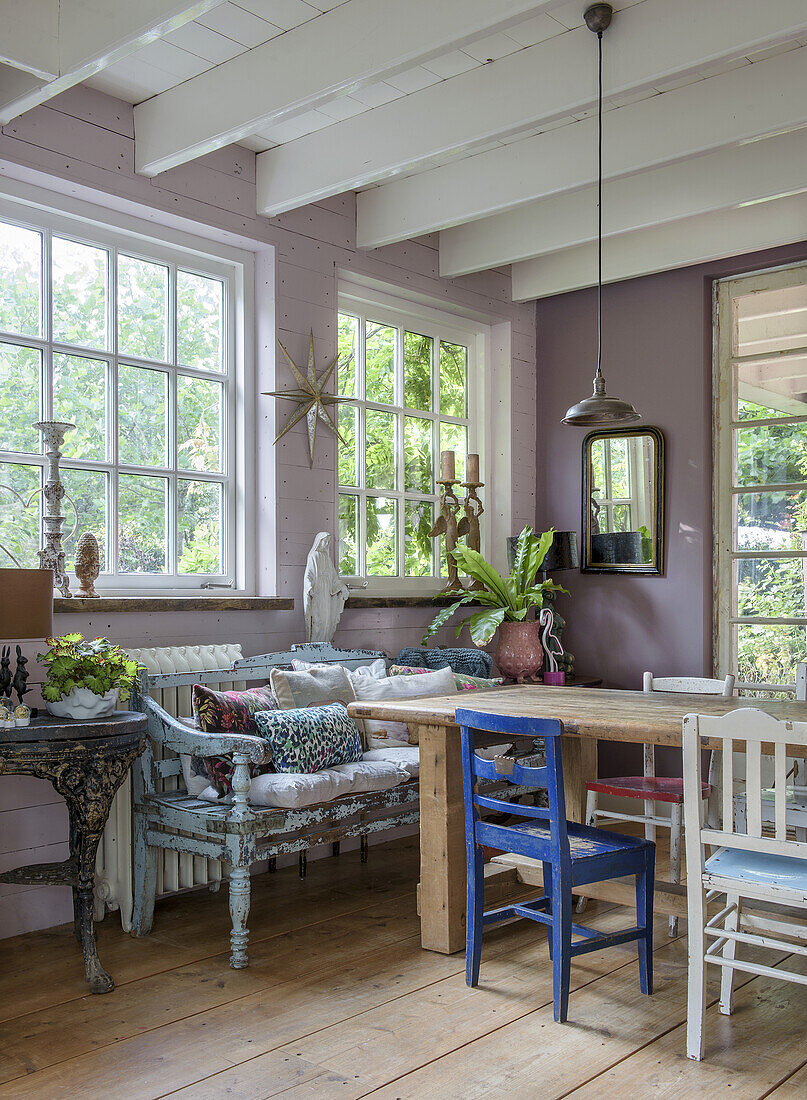 Dining room with wooden table, blue and white chairs, large mullioned windows and plants