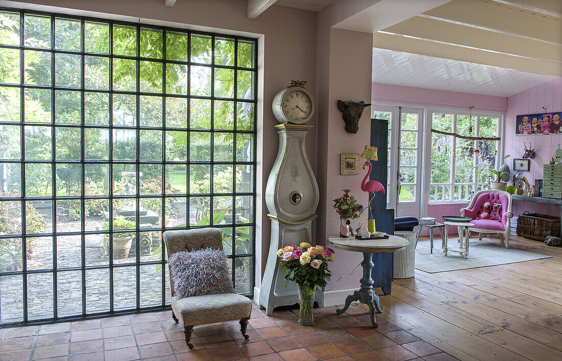 Living area with vintage furniture, grandfather clock and large mullioned windows overlooking the garden