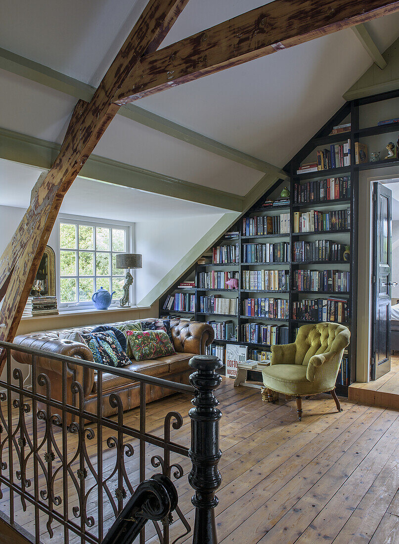 Open bookcase in the attic with leather sofa and armchair