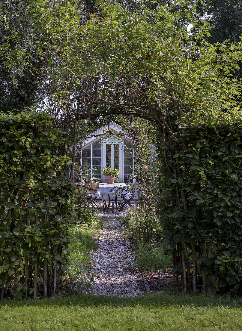 Garden path with gravel and arbour arch leading to a greenhouse with seating area