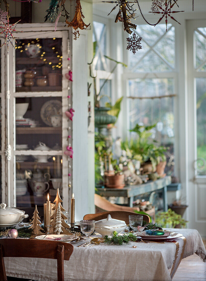 Gedeckter Tisch mit Kerzen und Weihnachtsdekoration in einem Wintergarten