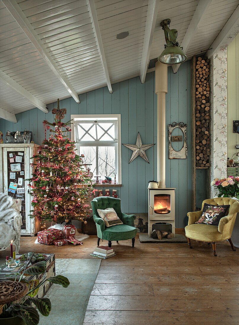 Wohnzimmer mit Holzofen, Weihnachtsbaum und Vintage-Sesseln vor hellblau gestrichener Holzwand