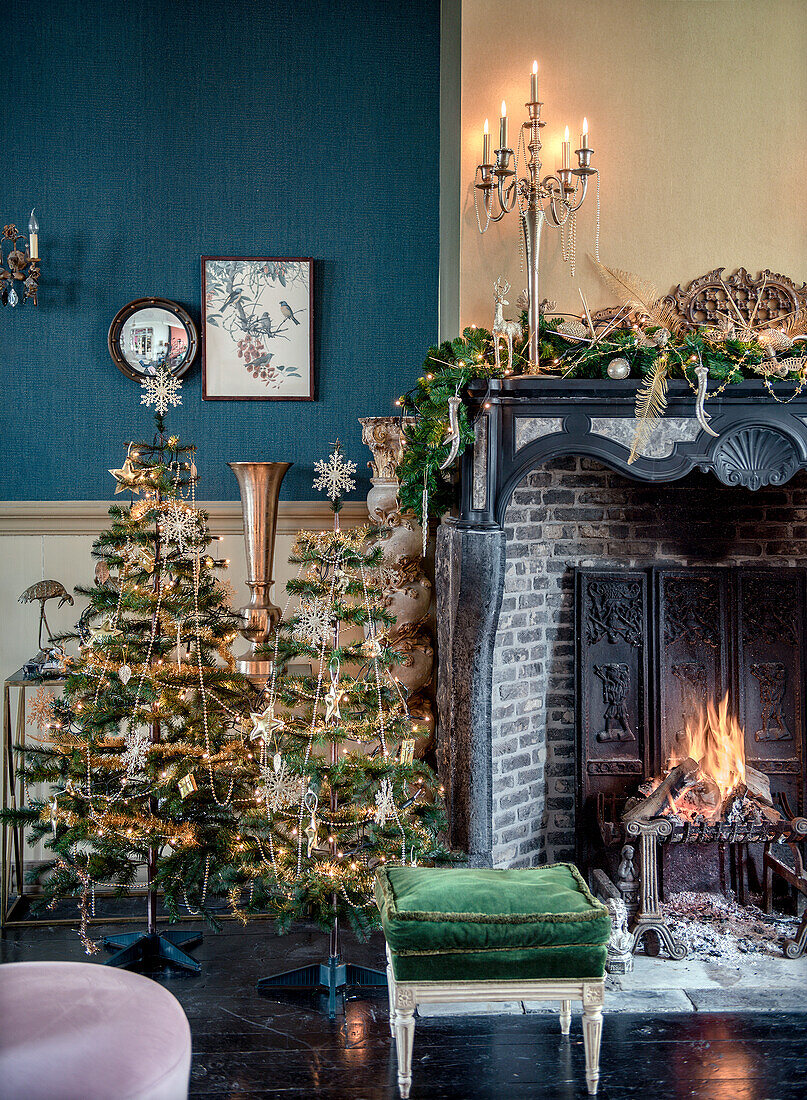 Weihnachtlich geschmückter Kamin in blau-gelbem Wohnzimmer mit Tannenbäumen und Kerzenleuchter