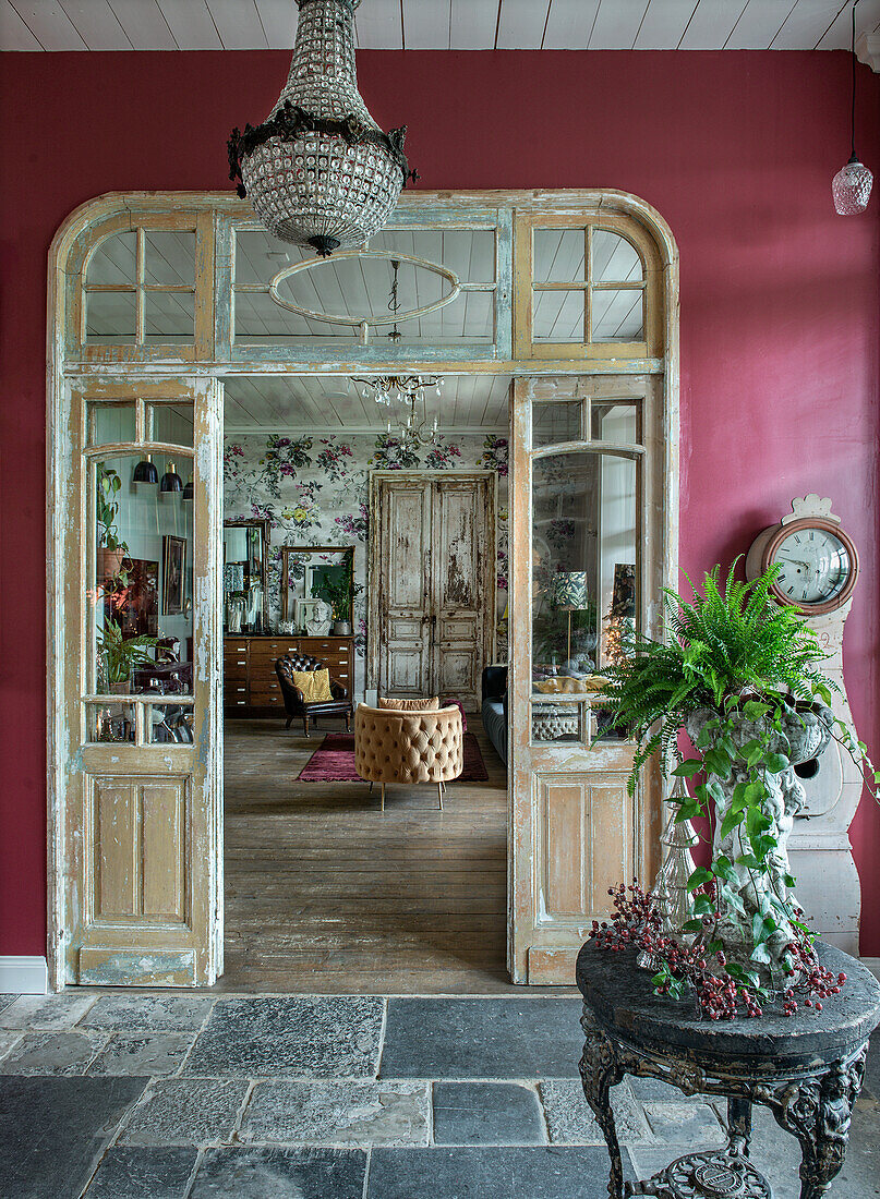 Historische Holzflügeltüren öffnen zu einem Salon mit floralen Tapeten und antiken Möbeln